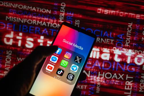 Social media icons logo displayed on a smartphone with disinformation on screen seen in the background, in this photo illustration. On 15 October 2023, in Brussels, Belgium. (Photo illustration by Jonathan Raa/NurPhoto)NO USE FRANCE