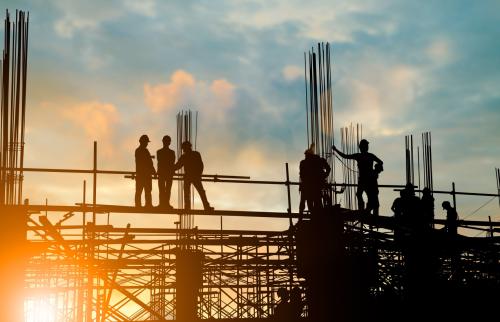 Construction workers on the scaffolding of a partially constructed building, silhouetted against the rising sun